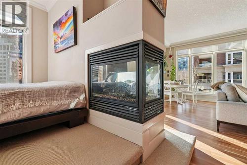 3 sided gas fireplace - 306, 660 Eau Claire Avenue Sw, Calgary, AB - Indoor Photo Showing Bedroom With Fireplace