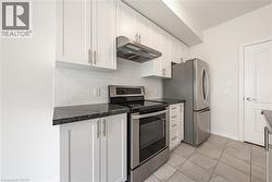 Kitchen featuring appliances with stainless steel finishes, white cabinetry, under cabinet range hood, and tasteful backsplash - 