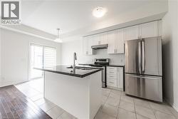 Kitchen with appliances with stainless steel finishes, white cabinetry, pendant lighting, and light tile patterned floors - 