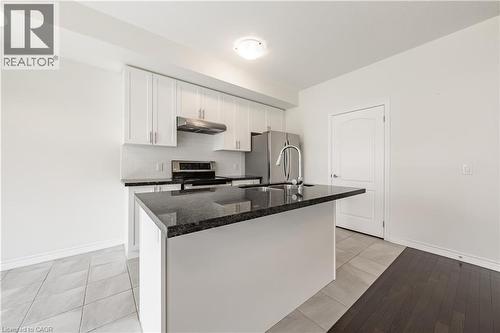 Kitchen with white cabinetry, light tile patterned floors, stainless steel appliances, under cabinet range hood, and dark stone countertops - 391 Athabasca Common, Oakville, ON - Indoor Photo Showing Kitchen With Double Sink With Upgraded Kitchen