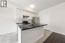 Kitchen with white cabinetry, light tile patterned floors, stainless steel appliances, under cabinet range hood, and dark stone countertops - 