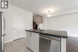 Kitchen featuring stainless steel appliances, white cabinetry, dark stone countertops, decorative light fixtures, and a kitchen island with sink - 