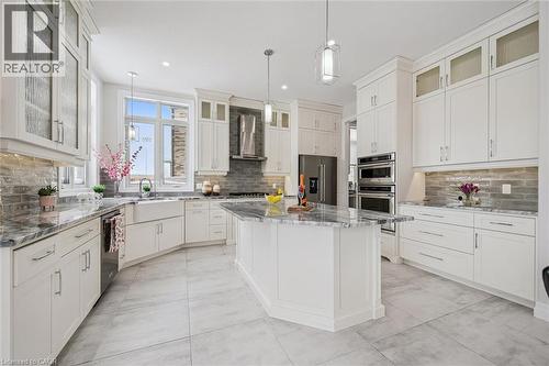 Kitchen featuring glass insert cabinets, appliances with stainless steel finishes, a center island, wall chimney exhaust hood, and light stone countertops - 263 Chestnut Ridge, Waterloo, ON - Indoor Photo Showing Kitchen With Upgraded Kitchen