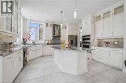 Kitchen featuring glass insert cabinets, appliances with stainless steel finishes, a center island, wall chimney exhaust hood, and light stone countertops - 