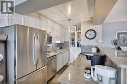 Kitchen with stainless steel appliances, decorative light fixtures, white cabinets, and light stone counters - 