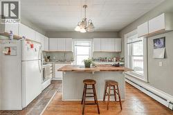 Kitchen with white appliances, wood counters, white cabinets, baseboard heating, and a breakfast bar - 