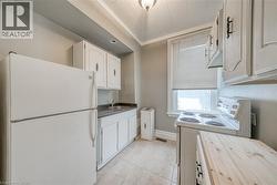 Kitchen featuring white appliances, ornamental molding, white cabinetry, wooden counters, and light tile patterned floors - 