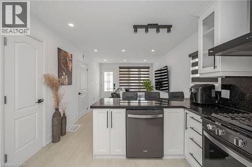 Kitchen with a peninsula, white cabinetry, wall chimney exhaust hood, appliances with stainless steel finishes, and dark stone counters - 525 Britannia Avenue, Hamilton, ON - Indoor Photo Showing Kitchen