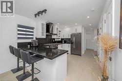 Kitchen featuring dark stone counters, stainless steel appliances, a kitchen breakfast bar, a peninsula, and wall chimney exhaust hood - 