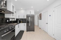 Kitchen featuring wall chimney range hood, stainless steel appliances, white cabinetry, recessed lighting, and light wood finished floors - 