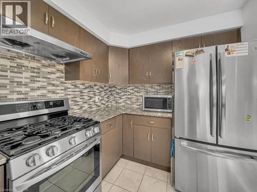 Kitchen with appliances with stainless steel finishes, ventilation hood, light stone counters, backsplash, and light tile patterned flooring - 144 Summit Ridge Drive, Guelph, ON - Indoor Photo Showing Kitchen With Stainless Steel Kitchen With Upgraded Kitchen