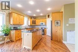 Kitchen featuring glass insert cabinets, dark countertops, light wood finished floors, a center island, and light brown cabinets - 