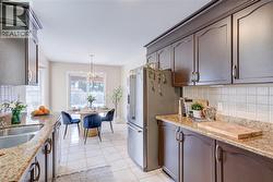 Kitchen with decorative backsplash, appliances with stainless steel finishes, light stone counters, a chandelier, and decorative light fixtures - 