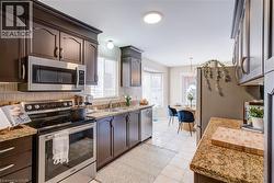 Kitchen featuring appliances with stainless steel finishes, light stone countertops, light tile patterned floors, dark brown cabinets, and a chandelier - 