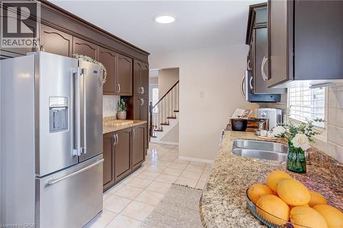 Kitchen featuring appliances with stainless steel finishes, backsplash, light stone counters, dark brown cabinets, and light tile patterned floors - 15 Claudette Gate, Hamilton, ON - Indoor Photo Showing Kitchen With Double Sink
