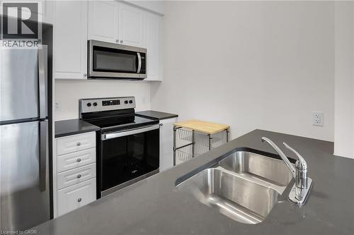 Kitchen with appliances with stainless steel finishes, white cabinetry, and dark stone countertops - 16 Concord Place Unit# 431, Grimsby, ON - Indoor Photo Showing Kitchen With Double Sink