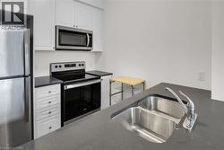 Kitchen with appliances with stainless steel finishes, white cabinetry, and dark stone countertops - 