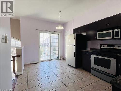 Kitchen with dark cabinetry, stainless steel appliances, pendant lighting, and light tile patterned floors - 5053 Bidwell Common, Burlington, ON - Indoor Photo Showing Kitchen