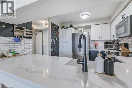 Kitchen with decorative backsplash, white cabinets, appliances with stainless steel finishes, a peninsula, and light stone counters - 3845 Lakeshore Boulevard W Unit# 804, Etobicoke, ON - Indoor