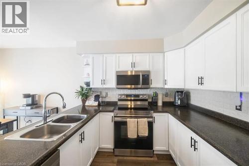 Kitchen featuring appliances with stainless steel finishes, white cabinetry, open shelves, decorative backsplash, and dark countertops - 25 Meadowvale Drive Unit# 3, Fonthill, ON - Indoor Photo Showing Kitchen With Double Sink
