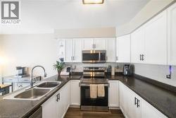 Kitchen featuring appliances with stainless steel finishes, white cabinetry, open shelves, decorative backsplash, and dark countertops - 