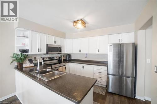 Kitchen featuring appliances with stainless steel finishes, open shelves, white cabinetry, a peninsula, and dark wood-style floors - 25 Meadowvale Drive Unit# 3, Fonthill, ON - Indoor Photo Showing Kitchen With Double Sink