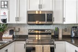 Kitchen featuring appliances with stainless steel finishes, white cabinets, open shelves, and backsplash - 