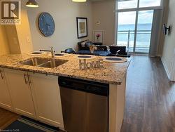 Kitchen featuring dishwasher, light stone counters, open floor plan, and dark wood-style floors - 