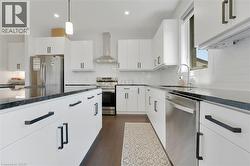 Kitchen with wall chimney range hood, stainless steel appliances, white cabinets, dark wood finished floors, and pendant lighting - 