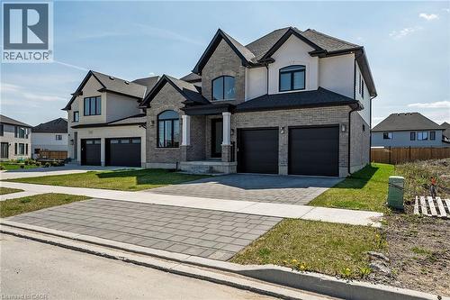 French country home featuring decorative driveway, brick siding, a garage, and stucco siding - 7266 Silver Creek Circle, London, ON - Outdoor With Facade