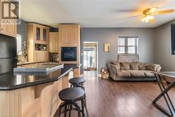 Kitchen featuring a breakfast bar area, light brown cabinetry, glass insert cabinets, black appliances, and dark wood-style flooring - 