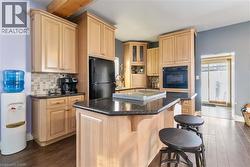 Kitchen featuring light brown cabinets, dark wood-type flooring, a kitchen breakfast bar, a center island, and black appliances - 