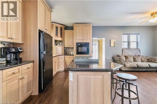 Kitchen with light brown cabinetry, glass insert cabinets, black appliances, open floor plan, and a kitchen island - 112 Eagle Avenue, Brantford, ON - Indoor Photo Showing Kitchen