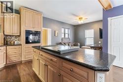 Kitchen featuring black oven, light brown cabinetry, ceiling fan, and dark wood finished floors - 