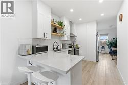 Kitchen featuring tasteful backsplash, open shelves, a peninsula, white cabinets, and appliances with stainless steel finishes - 