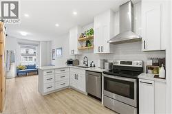Kitchen featuring stainless steel appliances, open shelves, a peninsula, wall chimney exhaust hood, and white cabinets - 