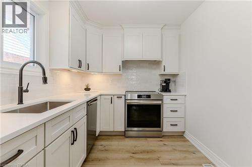 Kitchen featuring stainless steel appliances, light wood-style floors, white cabinets, light stone counters, and decorative backsplash - 5 Newport Lane, Port Dover, ON - Indoor Photo Showing Kitchen With Upgraded Kitchen
