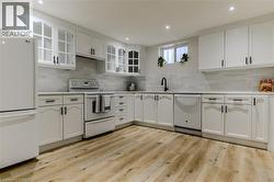 Kitchen with white appliances, white cabinetry, light wood-type flooring, light countertops, and recessed lighting - 