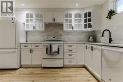 Kitchen featuring white appliances, white cabinetry, light wood-style floors, glass insert cabinets, and under cabinet range hood - 