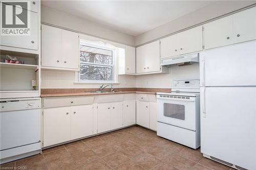Kitchen with white appliances, light countertops, under cabinet range hood, white cabinetry, and open shelves - 120 Fourth Avenue, Kitchener, ON - Indoor Photo Showing Kitchen With Double Sink