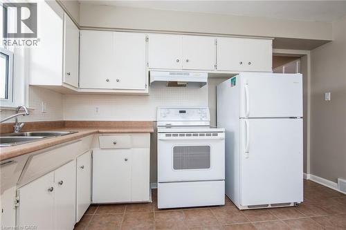 Kitchen with white appliances, white cabinets, light countertops, backsplash, and light tile patterned flooring - 120 Fourth Avenue, Kitchener, ON - Indoor Photo Showing Kitchen With Double Sink