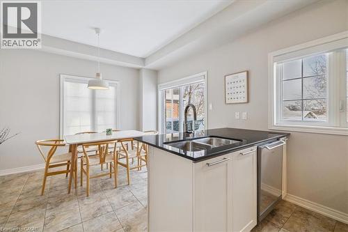 Kitchen featuring decorative light fixtures, dark stone countertops, stainless steel dishwasher, white cabinets, and plenty of natural light - 2220 Queensway Drive Unit# 15, Burlington, ON - Indoor Photo Showing Kitchen With Double Sink