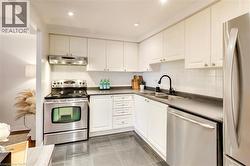 Kitchen with appliances with stainless steel finishes, dark countertops, under cabinet range hood, white cabinetry, and decorative backsplash - 