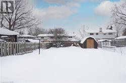 Yard covered in snow featuring a fenced backyard, a storage unit, and a residential view - 