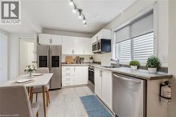 Kitchen featuring stainless steel appliances, white cabinetry, light wood-type flooring, and light countertops - 