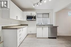 Kitchen featuring appliances with stainless steel finishes, white cabinets, light wood finished floors, and dark countertops - 