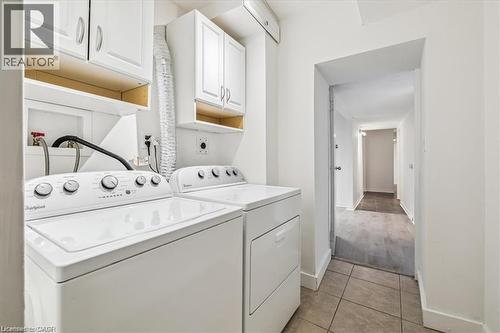 Laundry room with washing machine and dryer, cabinet space, and light tile patterned floors - 28 Grove Street, Hamilton, ON - Indoor Photo Showing Laundry Room
