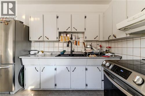 Kitchen with appliances with stainless steel finishes, white cabinetry, under cabinet range hood, tasteful backsplash, and light countertops - 126 Tisdale Street N, Hamilton, ON - Indoor Photo Showing Kitchen With Double Sink