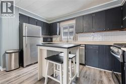 Kitchen featuring appliances with stainless steel finishes, dark cabinets, light wood-style flooring, and decorative backsplash - 