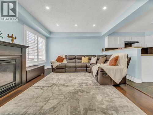 Living room with a tray ceiling, recessed lighting, dark wood-type flooring, a textured ceiling, and a glass covered fireplace - 29 Amsterdam Crescent, Guelph, ON - Indoor Photo Showing Living Room With Fireplace